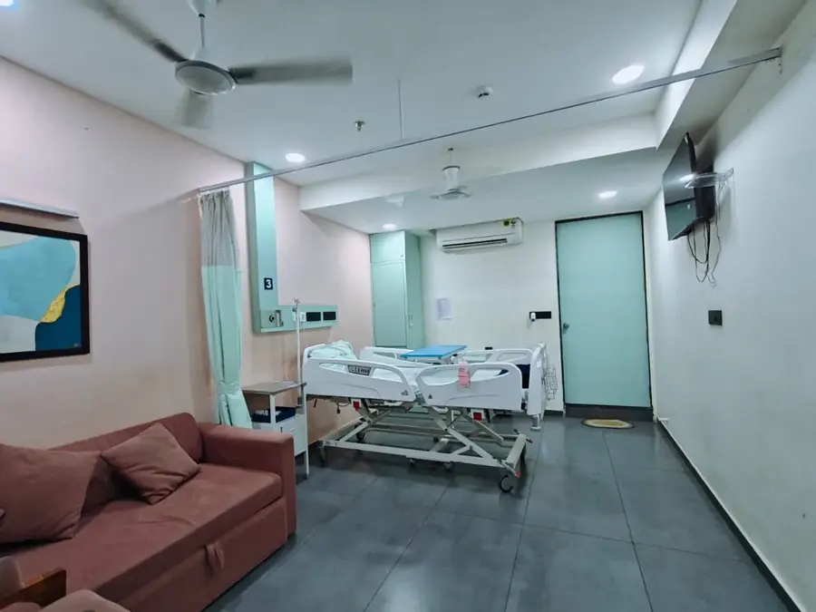Deluxe room with patient bed and attendant sofa at Pluto Hospital, Himatnagar